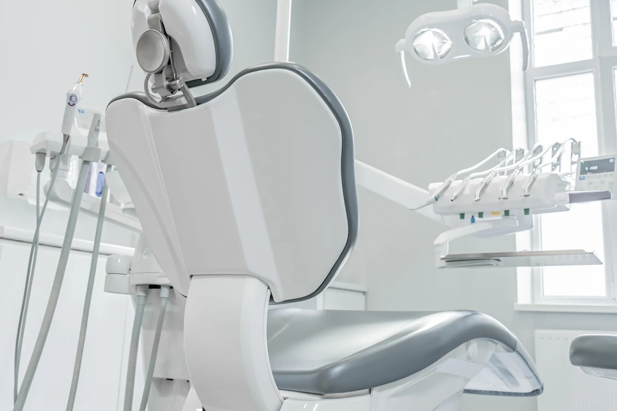 A treatment room with a white dental chair beside the window