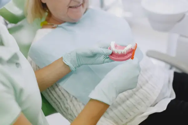 A dentist showing a senior patient how to care for her dentures