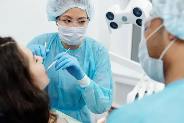 A dentist in protective gear examining a patient's mouth